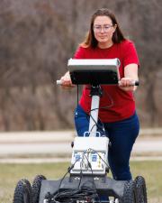 Researcher wearing a red shirt pusing a remote sensing machine in a field.